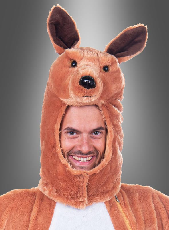 Eine Person lächelt, während sie das „Plüschmaske Känguru“-Set trägt, das aus einem waschbaren Schwanz und einem Beutel sowie Ohren und einem Gesicht an der Kapuze besteht und vor einem grauen Hintergrund mit Farbverlauf abgebildet ist.