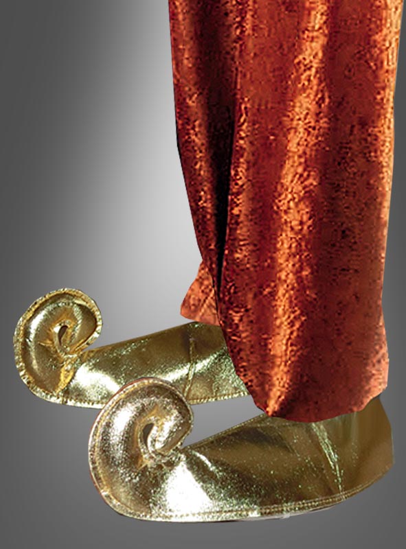 Eine Person in einer weiten orangefarbenen Hose und glänzenden goldenen „Wüstenprinz“-Schnabelschuh-Überzügen mit nach oben gebogenen Zehen, die an „1001 Nacht“ erinnern, steht vor einem neutralen Hintergrund.