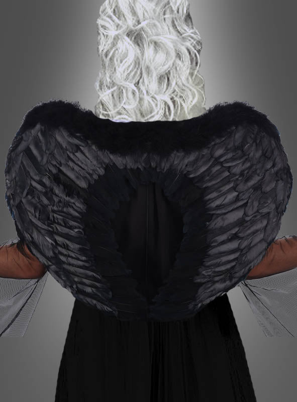 Eine Person mit weißem, lockigem Haar trägt die „Schwarzen Engelsflügel, beidseitig mit Federn, 60 cm“ sowie ein langes schwarzes Gothic-Kostüm und wurde von hinten vor einem neutralen grauen Hintergrund fotografiert.
