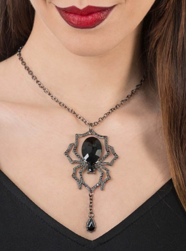 Eine Frau in einem schwarzen Oberteil und mit dunklem Lippenstift präsentiert die „Schwarze Spinne“-Halskette mit Edelstein, deren Blickfang eine markante schwarze Edelstein-Spinne mit einem herabhängenden, tropfenförmigen Edelstein ist – damit ist sie der perfekte Halloween-Schmuck.