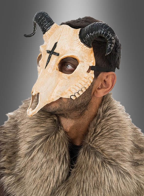 Ein Mann, der eine „Gehörnte Tierschädel-Halbmaske“ mit schwarzen Hörnern und einem Pelzkragen trägt und zur Seite blickt. Auf der Stirn der Maske ist ein markantes schwarzes Kreuz zu sehen.