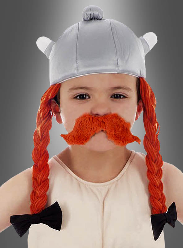 Ein Kind, das den „Obelix-Helm aus Stoff für Kinder“ trägt – einen silbernen Wikingerhelm mit Hörnern, orangefarbenen Zöpfen und einem orangefarbenen Schnurrbart –, steht vor einem grauen Hintergrund.