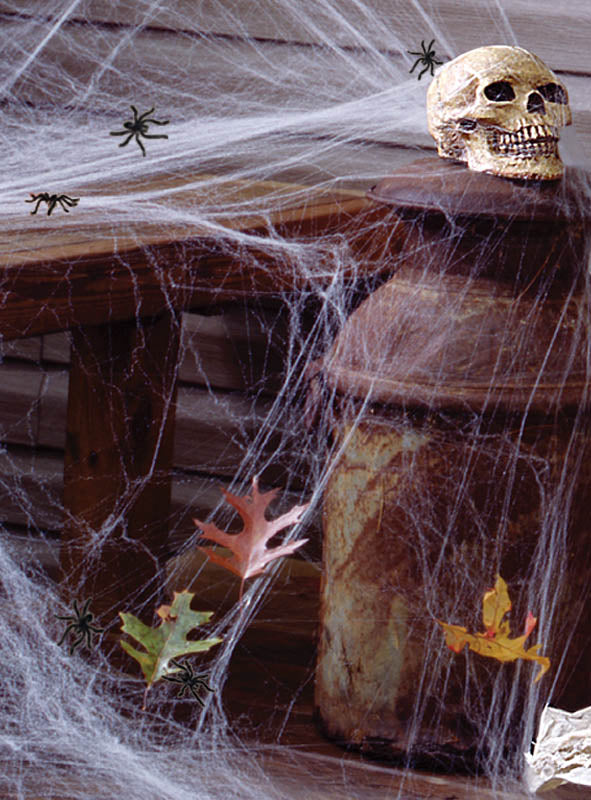 Ein Plastikschädel ruht auf einem rostigen Kanister, der mit „Leuchtendes Spinnennetz Halloween 60 g“-Spinnennetzen drapiert ist, dazwischen liegen Spielzeugspinnen und Papierblätter verstreut – eine ideale Ergänzung für Ihre Halloween-Dekoration.
