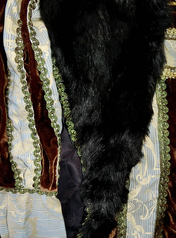 Nahaufnahme eines Kleidungsstücks aus braunem Samt, gemustertem blau-weißem Stoff, grüner Borte und einer drapierten schwarzen Pelzstola – ein elegantes Ensemble, das an das „Deluxe Großherzog Herrenkostüm“ erinnert.