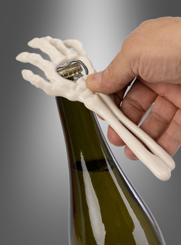 Eine Hand öffnet mit dem Halloween-Flaschenöffner „Skeletthand“, der die Form einer Skelett-Hand hat, eine Weinflasche vor einem grauen Hintergrund – das perfekte Accessoire für Ihre nächste Party.