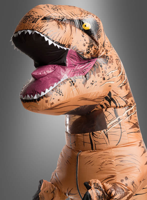 Eine Person, die ein aufblasbares Tyrannosaurus-Rex-Dinosaurierkostüm trägt, das sich durch ein offenes Maul mit rosa Innenseite und einen sichtbaren Reißverschluss auszeichnet, vor einem grauen Hintergrund mit Farbverlauf.