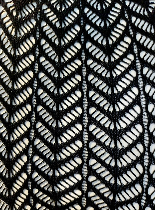 Nahaufnahme der Netzstrumpfhose mit Chevron-Muster, die sich durch schwarzen Spitzenstoff mit sich wiederholendem Chevron-Muster auszeichnet, dessen offene Stellen einen weißen Hintergrund durchscheinen lassen – ideal, um auffällige Statement-Stücke zu kreieren oder jedem Kostüm-Accessoire eine elegante Note zu verleihen.