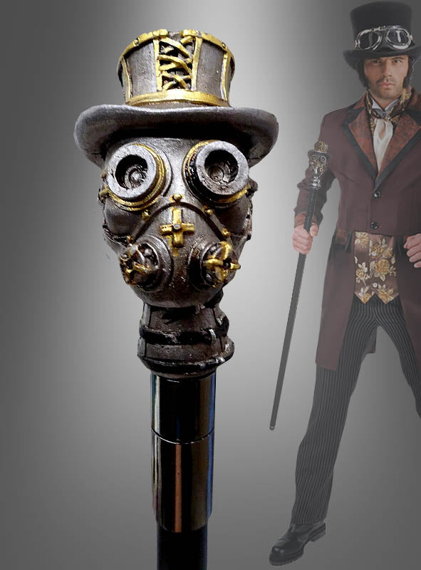 Im Hintergrund hält eine Person in einem Steampunk-Kostüm den „Deluxe Gehstock Steampunk“ – einen im Steampunk-Stil gestalteten Spazierstock mit einem Griff in Form einer Gasmaske, die einen Zylinder trägt – als auffälliges Kostümzubehör in der Hand.