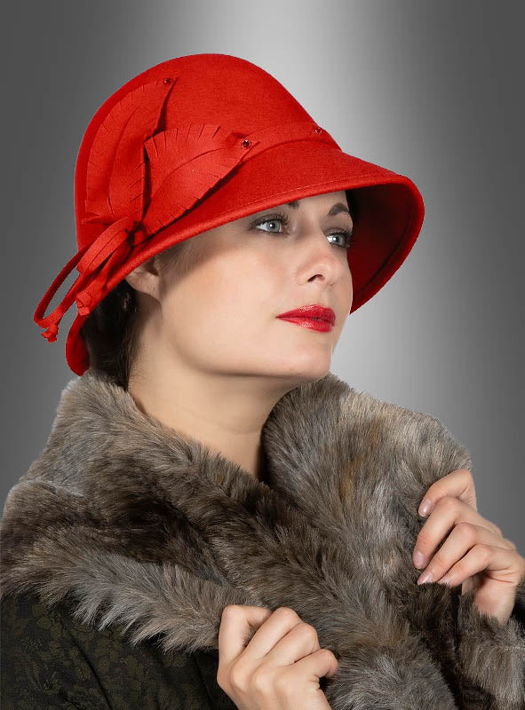 Eine Frau, die den „Roten Hut“ im Stil der 20er Jahre in Form eines Glockenhuts und eine Kunstfellstola trägt und vor einem grauen Farbverlaufshintergrund zur Seite blickt – eine elegante Hommage an die Vintage-Damenmode der 1920er Jahre.
