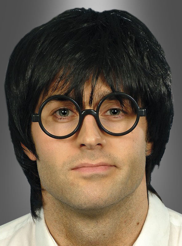 Eine Person, die die „Runde Brille Zauberlehrling“ in großer Größe und eine schwarze, mittellange Perücke trägt und vor einem schlichten grauen Hintergrund direkt in die Kamera blickt. Das Gesamtbild erinnert an ein klassisches Zauberlehrling-Kostüm.
