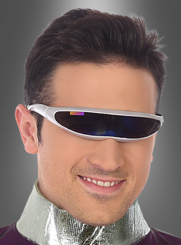 Ein Mann in einem Science-Fiction-Kostüm, komplett mit der Sonnenbrille der Zukunft „Space Weltall“ – einer futuristischen Sonnenbrille mit silbernem Rahmen – und einem glänzenden Metallkragen, lächelt vor einem grauen Hintergrund mit Farbverlauf.