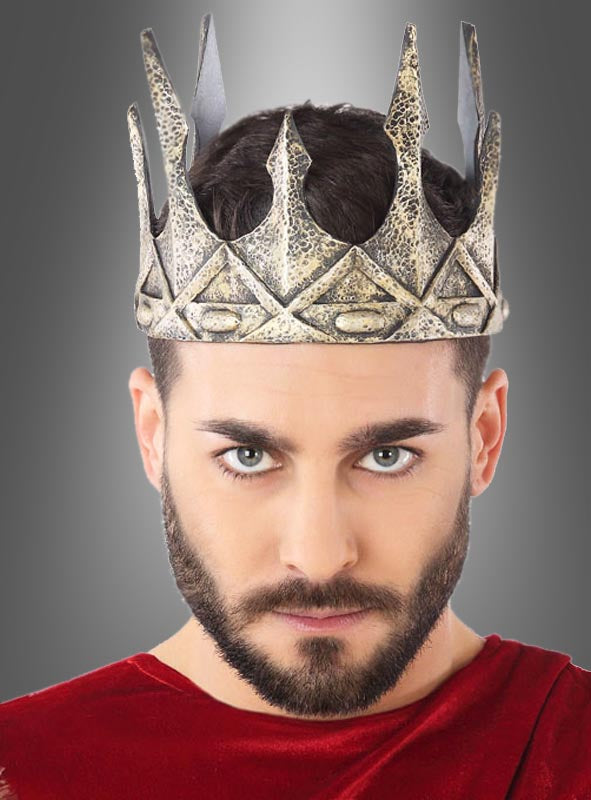 Ein Mann mit Bart und kurzen dunklen Haaren trägt die „Deluxe Latex Krone für Könige“ in Silbermetallic und ein rotes Gewand; er blickt mit ausdruckslosem Gesicht direkt in die Kamera.