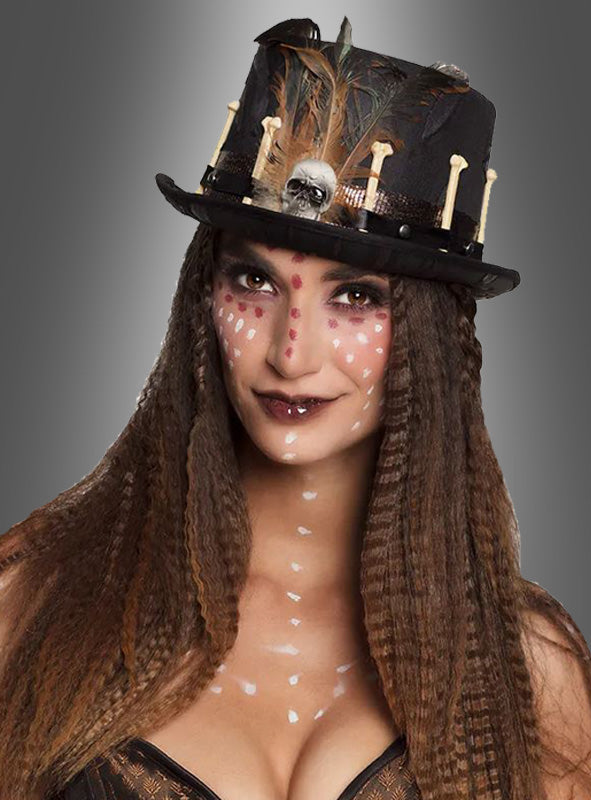 Vor einem grauen Hintergrund steht eine Frau, die den „Voodoo-Zylinder mit Knochen & Feder“ trägt, langes, gekräuseltes Haar hat und deren Gesicht weiß und rot bemalt ist.