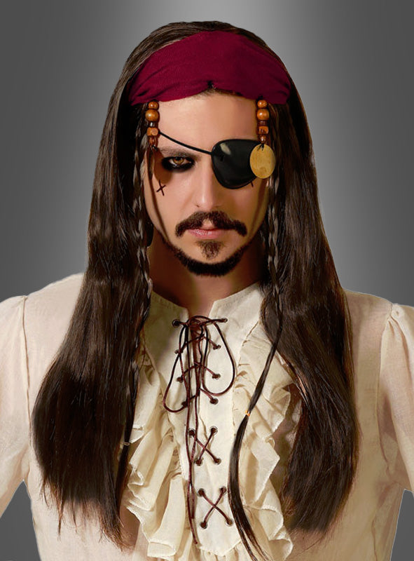 Eine Person in einem Piratenkostüm mit einem Rüschenhemd, einer langen braunen Piratenperücke mit Stirnband und Perlen, einer schwarzen Augenklappe und einem dunklen Bart vor einem grauen Hintergrund mit Farbverlauf.