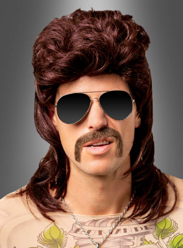 Eine Person, die die rotbraune Herrenperücke „80er Vokuhila“, eine Pilotenbrille und einen falschen Schnurrbart trug sowie eine Halskette und ein Shirt mit Tattoo-Motiv, posierte vor einem grauen Hintergrund mit Farbverlauf.