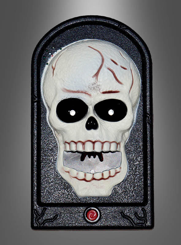 Die „Türklingel Skelett Totenschädel Halloween“ ist in einen schwarzen, gewölbten Rahmen mit einem roten Knopf an der Unterseite eingefasst und verfügt über einen Kunststoffschädel mit markanten schwarzen Augenhöhlen und leuchtend roten Rissen – damit ist sie ein auffälliges Halloween-Dekostück mit Totenschädel-Motiv oder ein Akzent im Horror-Stil für Ihren Eingangsbereich, hier abgebildet vor einem grauen Hintergrund mit Farbverlauf.