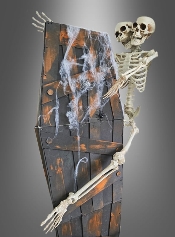 Aus dem „Rüttelnder Halloween-Sarg mit Ketten 160 cm“ – einem Holzsarg, der mit künstlichen Spinnweben, Ketten und einer Plastikspinne verziert ist und vor einem grauen Hintergrund steht – ragen zwei Skelette mit miteinander verwachsenen Oberkörpern und Köpfen hervor – eine beunruhigende Szene, die sich perfekt für jede gruselige Halloween-Dekoration eignet.