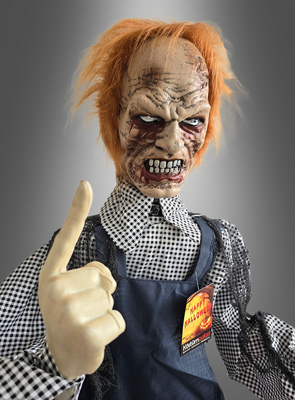 Eine furchteinflößende Halloween-Dekoration, der „Zombie-Totengräber mit Schaufel 160 cm, animiert“, zeigt einen animatronischen Zombie-Totengräber mit zerzaustem orangefarbenem Haar, einem vernarbten Gesicht und einem erhobenen Zeigefinger, der ein kariertes Hemd und eine Schürze trägt und ein „Happy Halloween“-Anstecker.