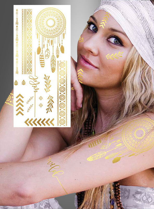 Eine Frau trägt „Hippie Boho Tattoo Abziehbilder Gold“ – darunter einen Traumfänger und andere Boho-Motive – sowie ein Kopftuch und eine Perlenkette; sie sitzt mit erhobenem Arm da; im Vordergrund ist das goldene Tattoo-Bogen zu sehen.