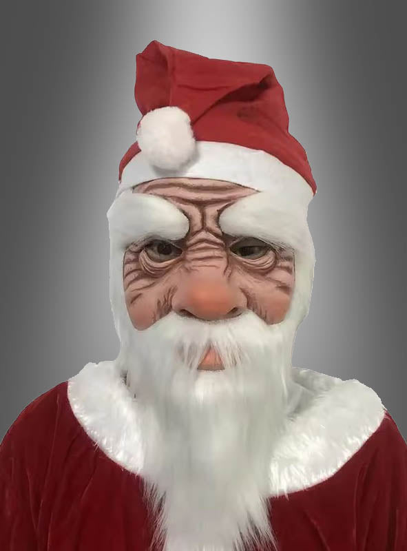 Eine als Weihnachtsmann verkleidete Person, die eine Latexmaske mit Mütze trägt, die durch übertriebene Falten und einen weißen Bart gekennzeichnet ist, vor einem grauen Hintergrund mit Farbverlauf.
