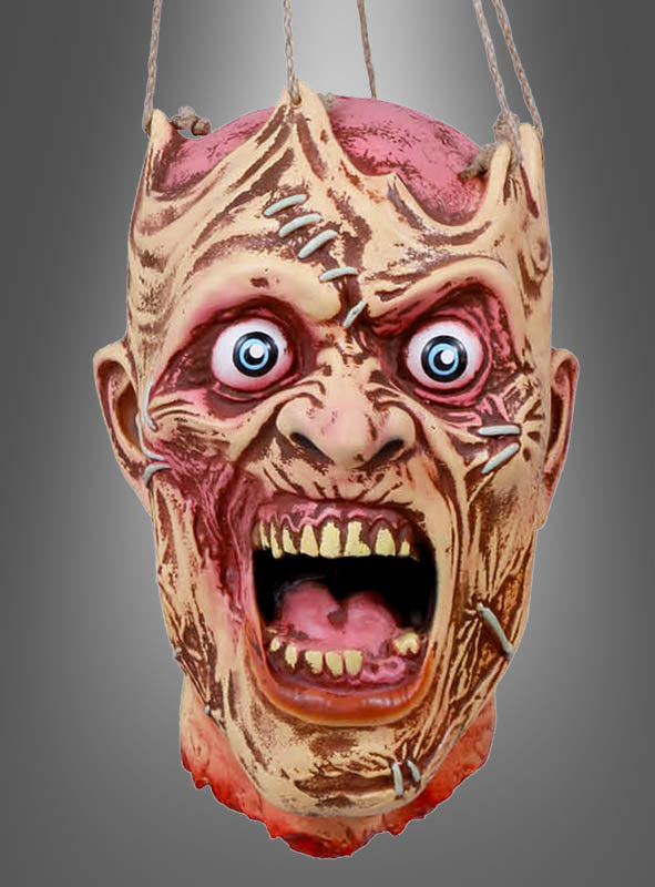 Eine gruselige Maske mit weit aufgerissenen Augen, die einen aufgehängten Zombiekopf mit Nähten, Wunden und einem klaffenden Mund darstellt, hängt an zwei Seilen vor einem grauen Hintergrund mit Farbverlauf – ein furchterregender Monsterkopf zum Aufhängen, perfekt für deine Halloween-Deko.