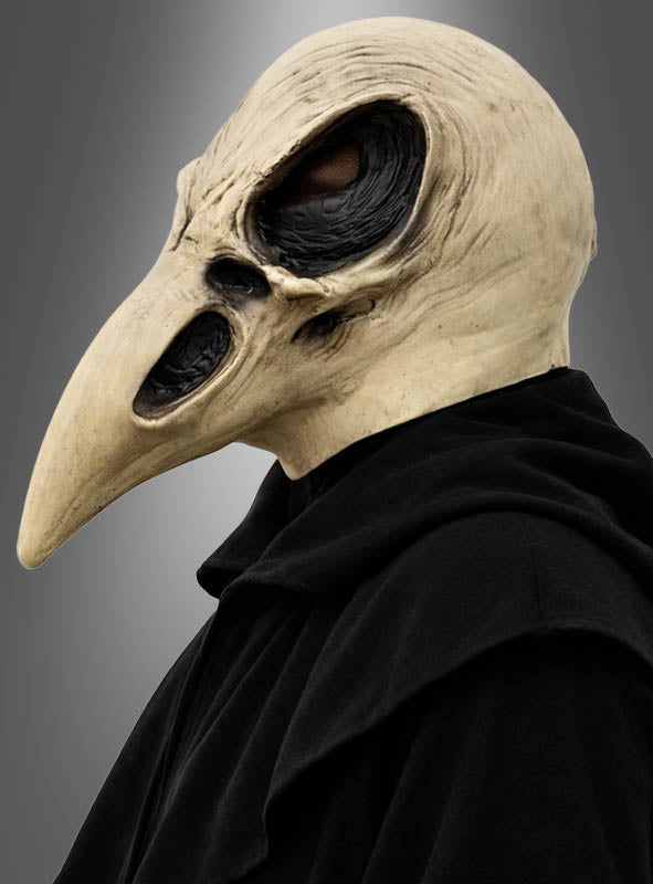 Eine Person, die eine „Krähen Schädel“-Halloween-Maske trägt – mit einem detailreichen Design mit langem Schnabel und dunklen Augenöffnungen –, gekleidet in einen schwarzen Umhang vor einem neutralen Hintergrund mit Farbverlauf.