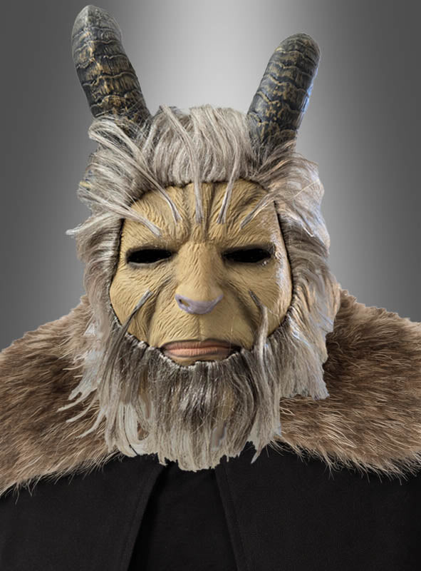 Vor einem grauen Farbverlaufshintergrund ist eine Person zu sehen, die die „Biest Vollmaske mit Hörner Krampus“ trägt, die mit ziegenartigen Hörnern, Fellverzierungen und einem braunen Umhang ausgestattet ist.