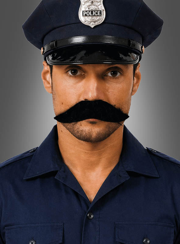 Ein Mann in einer dunkelblauen Polizeiuniform und einer Mütze mit Polizeimarke, der einen großen schwarzen Schnauzer-Oberlippenbart trägt, blickt vor einem schlichten grauen Hintergrund nach vorne.
