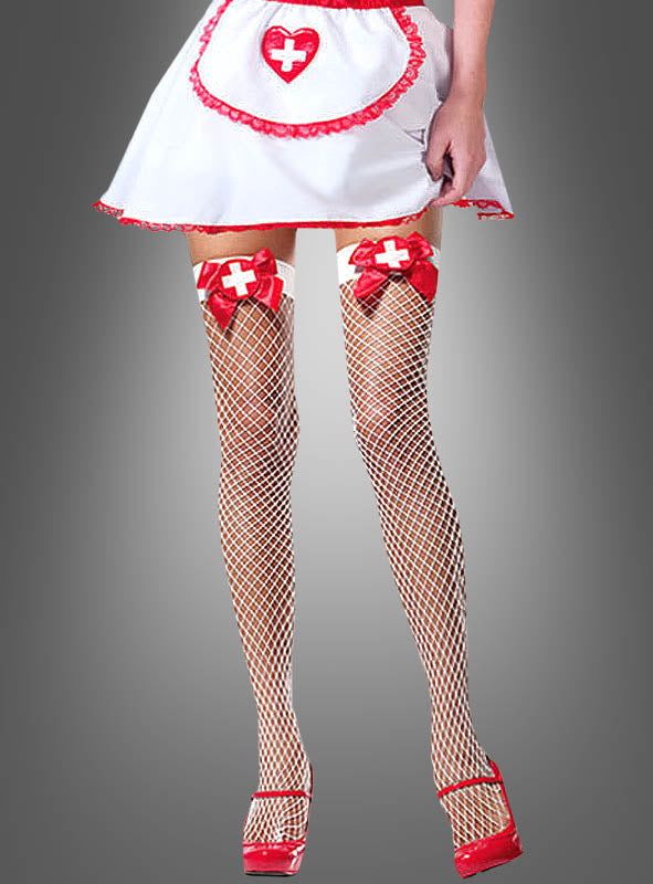 Sie trägt ein kurzes weißes Krankenschwester-Kostüm mit einer Schürze und präsentiert vor einem grauen Hintergrund sexy Krankenschwester-Netzstrümpfe – weiße halterlose Strümpfe mit roten Schleifen und Kreuzen – sowie auffällige rote Stöckelschuhe.