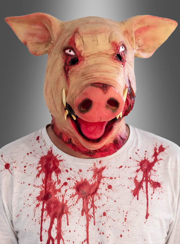 Eine Person trägt die „Blutige Latexmaske Schwein“ und ein weißes Hemd mit roten Spritzern und steht vor einem grauen Hintergrund mit Farbverlauf. Diese gruselige Halloween-Maske sorgt für eine unheimliche, beunruhigende Wirkung, die sich perfekt für gruselige Anlässe eignet.