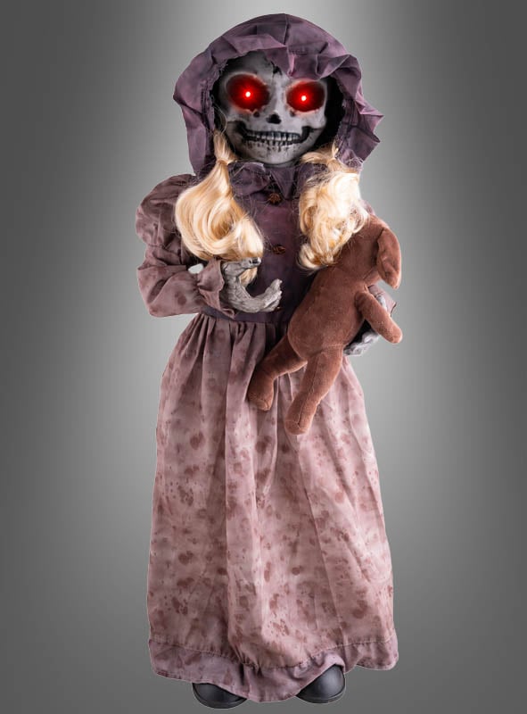 Die „Horror-Puppe 95 cm mit drehbarem Kopf“ ist eine Skelettpuppe mit leuchtend roten Augen, langen blonden Haaren, einer lila Haube und einem altmodischen Kleid, die ein braunes Stofftier im Arm hält. Diese animierte Halloween-Dekoration verfügt über einen drehbaren Kopf, der Ihrer Grusel-Dekoration einen besonders unheimlichen Effekt verleiht.