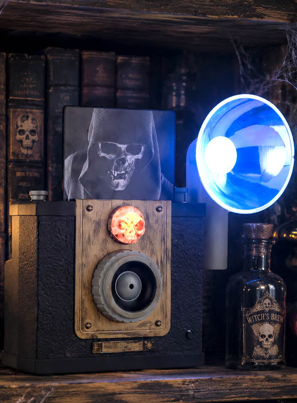Die „Geister Fotoapparat 24 cm mit Licht animiert“ projiziert ein gruseliges Totenkopfbild und schafft so die perfekte Kulisse für eine unheimliche Halloween-Dekoration. Umgeben Sie ihn mit antiken Büchern, deren Buchrücken mit Totenkopfmotiven verziert sind, einem blau leuchtenden Horn und einer Glasflasche mit der Aufschrift „Witch’s Brew“ für die ultimative gruselige Deko – perfekt für jeden Fan von stimmungsvoller Halloween-Dekoration.