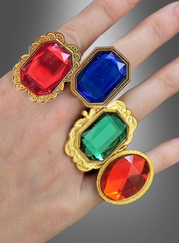 Eine Hand hält vier „Goldene Ringe mit Edelstein, verstellbar“ in die Hand, die jeweils mit großen roten, blauen, grünen und orangefarbenen Edelsteinen besetzt sind – darunter ein auffälliger Edelsteinring – vor einem grau verlaufenden Hintergrund. Ideal als Kostümschmuck für den Karneval oder um jedem Anlass das gewisse Etwas zu verleihen.