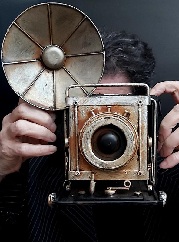 Eine Person, die den „Retro Fotoapparat mit Blitz Deko Kamera“ mit seinem großen runden Blitz nach vorne gerichtet in der Hand hält – ein idealer Vintage-Deko-Akzent für jede 20er-Jahre-Party.