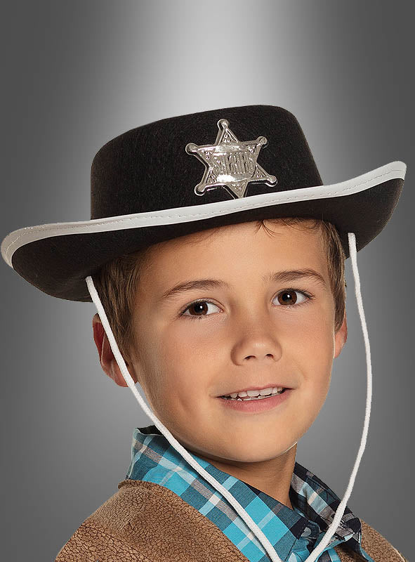 Ein kleiner Junge mit einem Cowboyhut mit Sheriffstern für Kinder, dazu ein kariertes Hemd und eine braune Jacke – er lächelt vor einem grauen Hintergrund: das perfekte Cowboykostüm für kleine Abenteurer.
