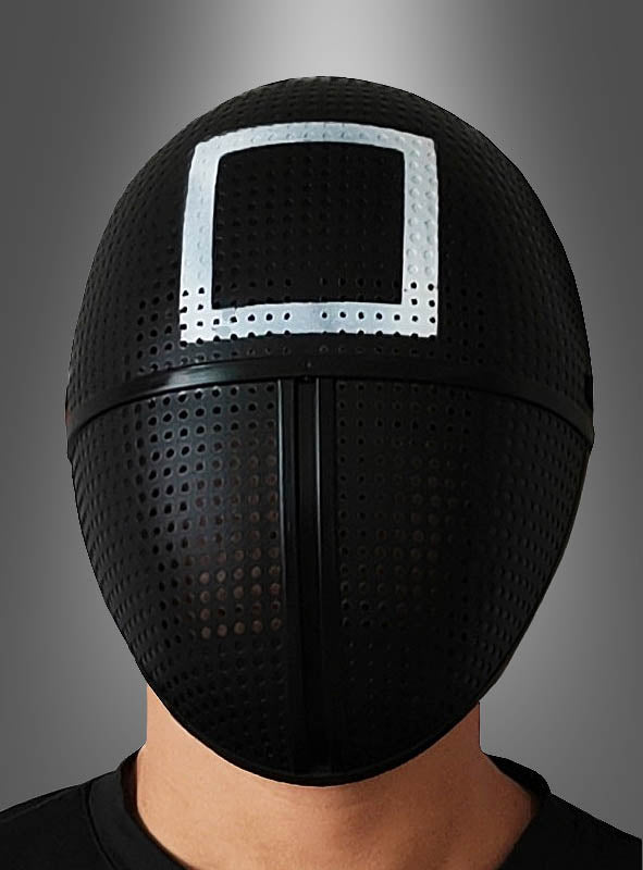Eine Person, die eine schwarze „Game Aufseher Maske Viereck Quadrat“ trägt, auf deren Stirn ein weißes quadratisches Symbol vor einem grau verlaufenden Hintergrund zu sehen ist.