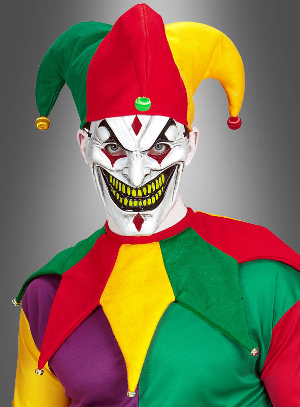 Eine Person trägt das farbenfrohe Unisex-Kostümset „Narrenkappe und Kragen“, komplett mit einer gruseligen Maske mit breitem, zahnigem Grinsen, weißer Gesichtsbemalung sowie gelben und grünen Akzenten. Das auffällige Ensemble umfasst den klassischen Narrenkragen und die leuchtende Kappe, alles vor einem grauen Hintergrund mit Farbverlauf.