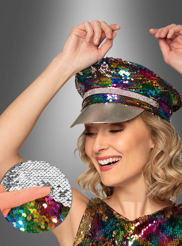 Eine lächelnde Person trägt die „Wende-Pailletten-Mütze Festival Style“ und ein buntes Pailletten-Oberteil. In einer Nahaufnahme ist zu sehen, wie ein Finger die Pailletten auf der Mütze von silberfarben auf bunt umdreht – damit ist sie die perfekte, schimmernde Wahl für jedes Festival-Outfit.