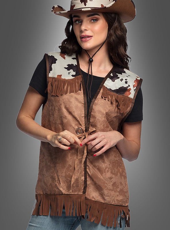 Eine Person, die einen braunen Cowboyhut, ein schwarzes T-Shirt und die „Cowboy Weste für Damen“ mit Kuhmuster an den Schultern trägt, posiert vor einem grauen Hintergrund und sorgt so für einen authentischen Western-Look.