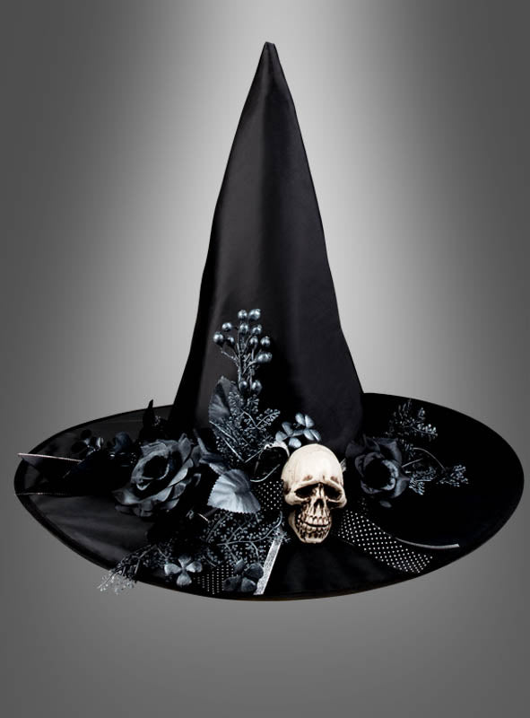 Die „Halloween-Hut für Hexen mit Totenkopf-Blumenschmuck“ ist ein schwarzer, spitzer Hexenhut, ideal für Ihr Halloween-Kostüm oder Hexenkostüm, verziert mit schwarzen Kunstblumen, Blättern, Beeren, einer Schleife und einem kleinen Totenkopf-Ornament an der Krempe, dargestellt vor einem grauen Hintergrund mit Farbverlauf.
