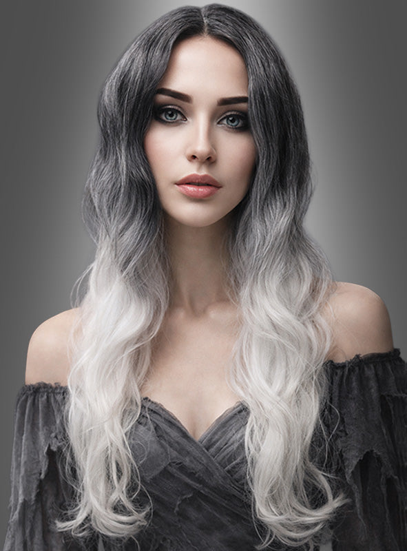 Eine Frau mit langen, welligen Haaren in einem Schwarz-zu-Weiß-Ombré-Look, die die Lockenperücke „Geisterdame weiß-schwarz“ trägt, und hellen Augen steht in einem schulterfreien dunklen Kleid vor einem grauen Hintergrund mit Farbverlauf.