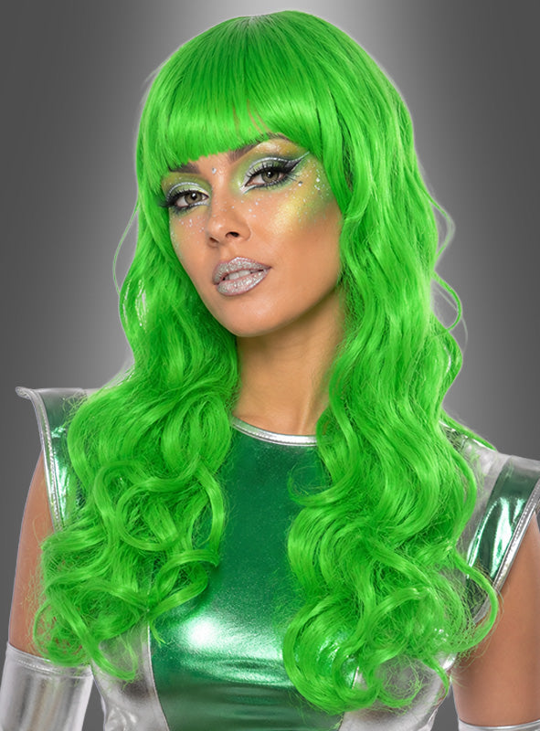 Eine Person mit langen, welligen, neongrünen Haaren, gestylt mit der „Lange Lockenperücke Alien grün“, und auffälligem Metallic-Make-up, die ein glänzendes grün-silbernes Outfit trägt, das an eine Meerjungfrau erinnert, und vor einem grauen Hintergrund mit Farbverlauf posiert.