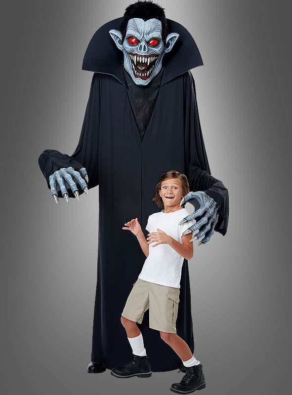 Ein Kind steht vor einer hoch aufragenden, bedrohlichen Gestalt, die das „Gigantische Vampir-Kostüm oder Deko, ca. 240 cm“ trägt – mit scharfen Zähnen, roten Augen, blauer Haut und langen Krallen – ideal für jede Halloween-Verkleidung. Die gruselige Szene spielt sich vor einem schlichten grauen Hintergrund ab.