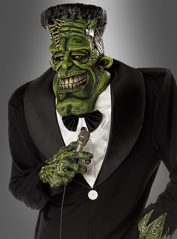 Im „Big Franky Monsterkostüm mit übergroßer Maske“ hält eine Person mit einer grünen Frankenstein-Monster-Maske und einem entsprechenden Kostüm ein Mikrofon in der Hand; sie trägt einen schwarzen Smoking mit Fliege vor einem grauen Hintergrund – perfekt für jede Themenveranstaltung und erhältlich in den Herrengrößen L–XL.