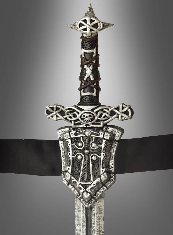 Das „Ritterschwert mit Gürtel, 60 cm“ ist ein Schwert im mittelalterlichen Stil mit einem kunstvoll verzierten Griff, der mit keltischen Knotenmustern, einem Totenkopf und einer dekorativen Parierstange verziert ist – perfekt für jedes Mittelalterkostüm oder jede Karnevalsveranstaltung – und wurde vor einem grauen Hintergrund mit Farbverlauf fotografiert.