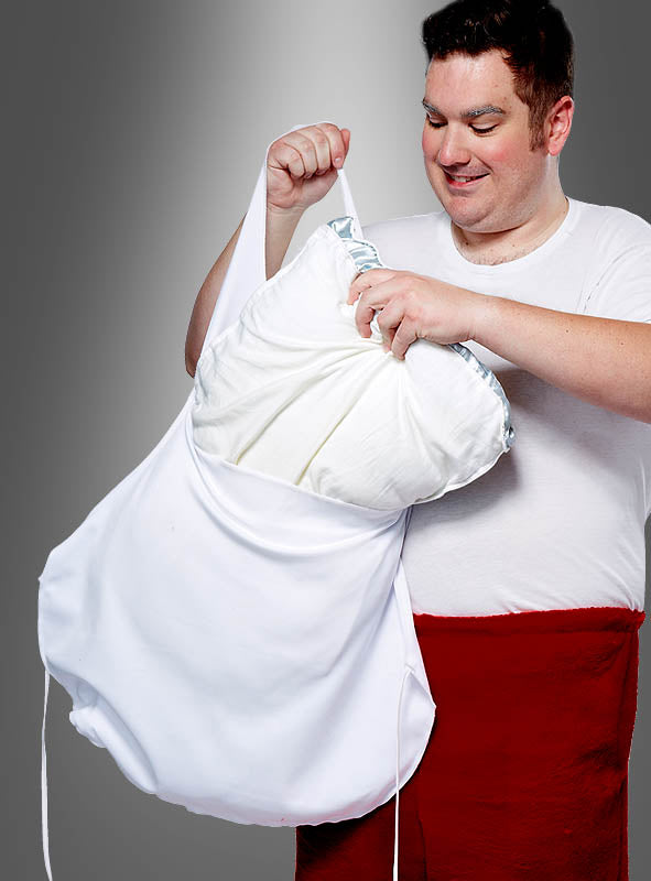 Ein Mann in einem weißen Hemd und einer roten Schürze für den dicken Nikolausbauch legt ein Kissen in einen übergroßen weißen Kissenbezug oder Wäschebeutel vor einem grauen Hintergrund und demonstriert so die Verwendung dieses „Fake-Bauch“-Accessoires als lustiges Kostümzubehör.