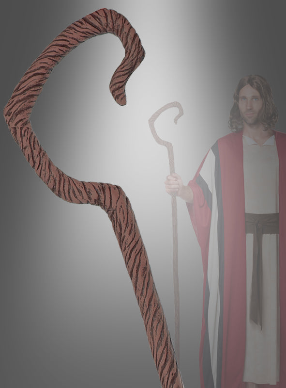 Eine Person in einem rot-weißen Gewand hält den „Hirtenstab Deluxe“ in Braun (165 cm) in der Hand – einen großen, geschwungenen Stab mit auffälligem Design, der im Vordergrund deutlich zur Geltung kommt und somit ein markantes Kostüm-Accessoire darstellt, das jedem Karnevalskostüm das gewisse Etwas verleiht.