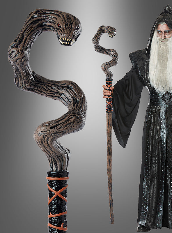 Ein Zauberer in einer schwarzen Robe hält den „Fantasy Stab mit Schlangenkopf 150 cm“ in der Hand, dessen gewundener, schlangenförmiger Kopf mit roten Augen und scharfen Zähnen sich deutlich von einem grauen Hintergrund mit Farbverlauf abhebt – ein perfektes Voodoo-Zauberer-Accessoire für Halloween-Zauber.