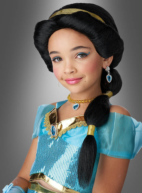 Ein junges Mädchen trägt ein blau-goldenes „Wüstenprinzessin“-Kostüm mit Schmuck, eine gestylte Frisur unter einer „Arabische Prinzessin“-Kinderperücke und ein dezentes Make-up und posiert vor einem schlichten grauen Hintergrund.