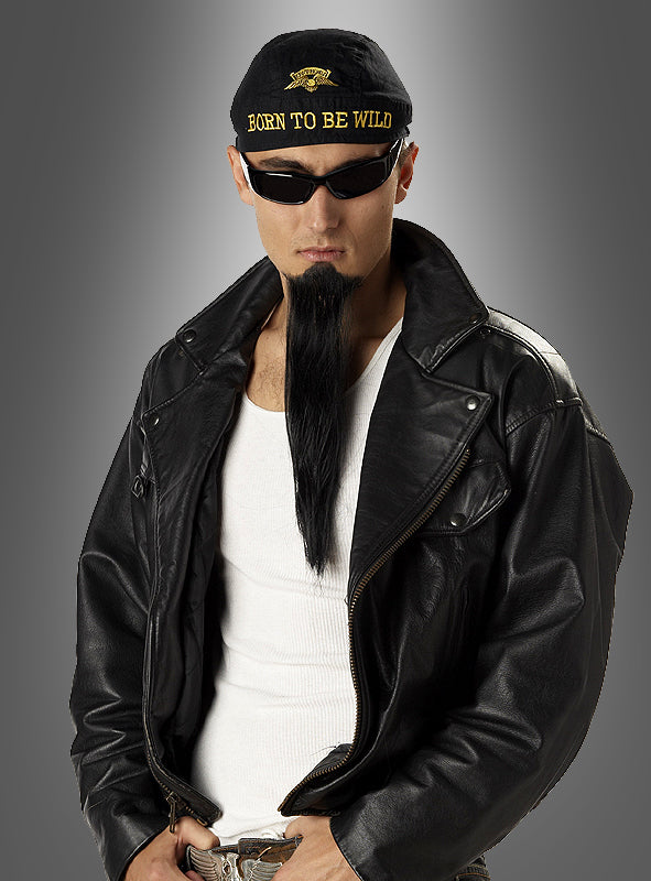 Vor einem grauen Hintergrund steht ein Mann, der eine schwarze Lederjacke, eine Sonnenbrille und eine Kappe mit der Aufschrift „Born to be Wild“ trägt. Seinen klassischen Metal-Look rundet er mit dem unverkennbaren „Cooler Langer Rocker“-Kinnbart ab, der den echten Biker-Bart-Stil verkörpert.